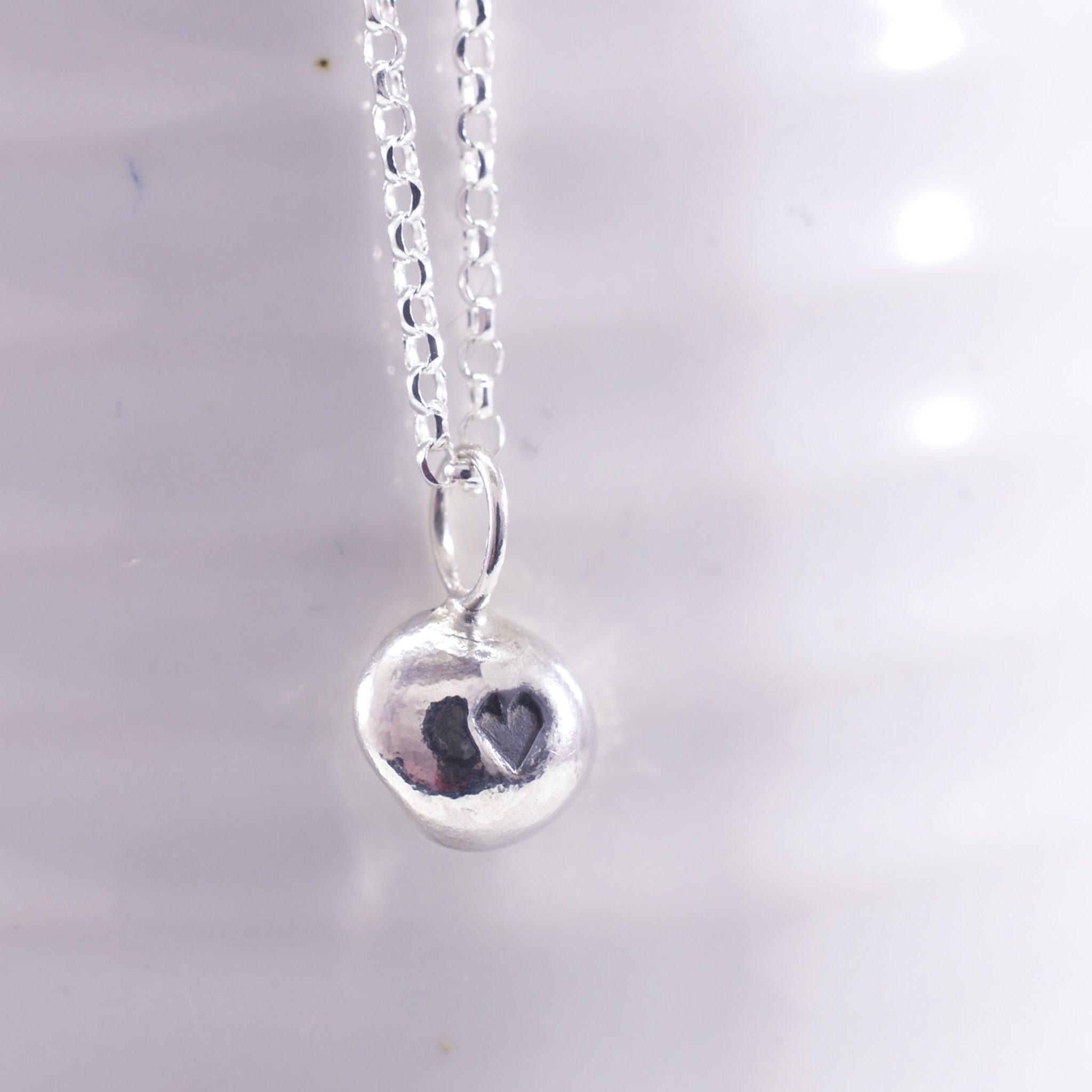 Organic shaped silver pebble necklace with black heart to centre