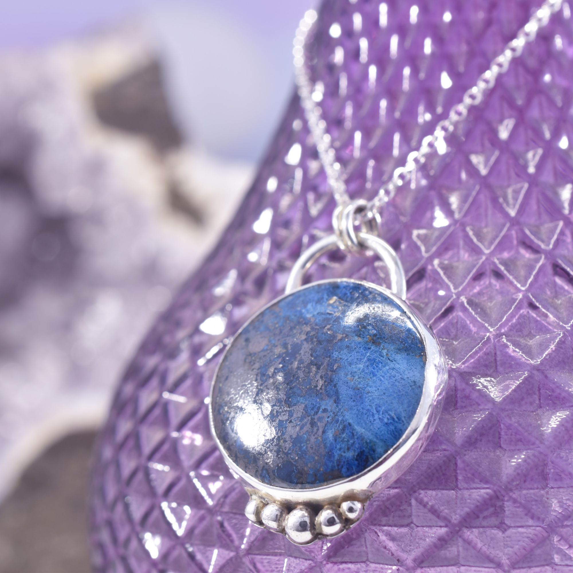 A round disc of deep blue and dark copper Shattuckite, set in a sterling silver surround with 5 graduated solid silver balls to the base.