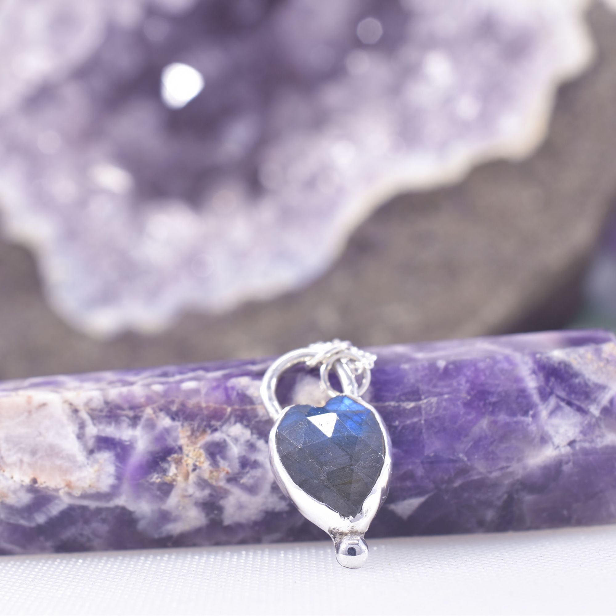 a heart of faceted blue flash labradorite, set in sterling silver and featuring a solid silver ball at the base. A heart cut out to the reverse allows the light to shine through the stone.