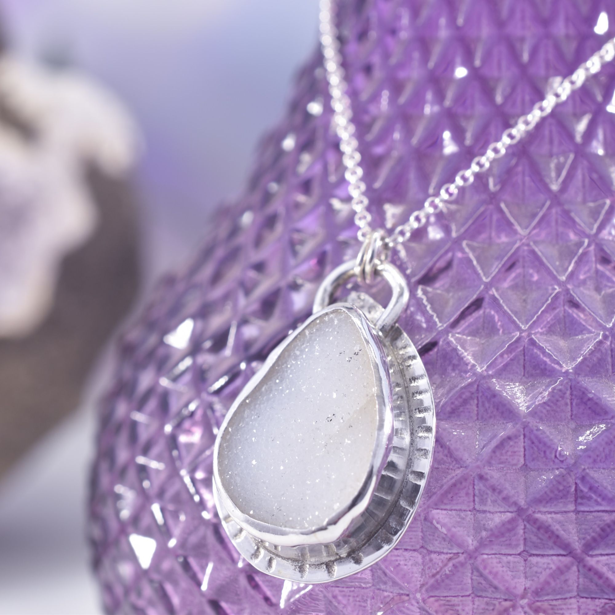 A teardrop of raw crystal druzy quartz, set within sterling silver, with a radiant lined border. The back features a moon and crystal design.
