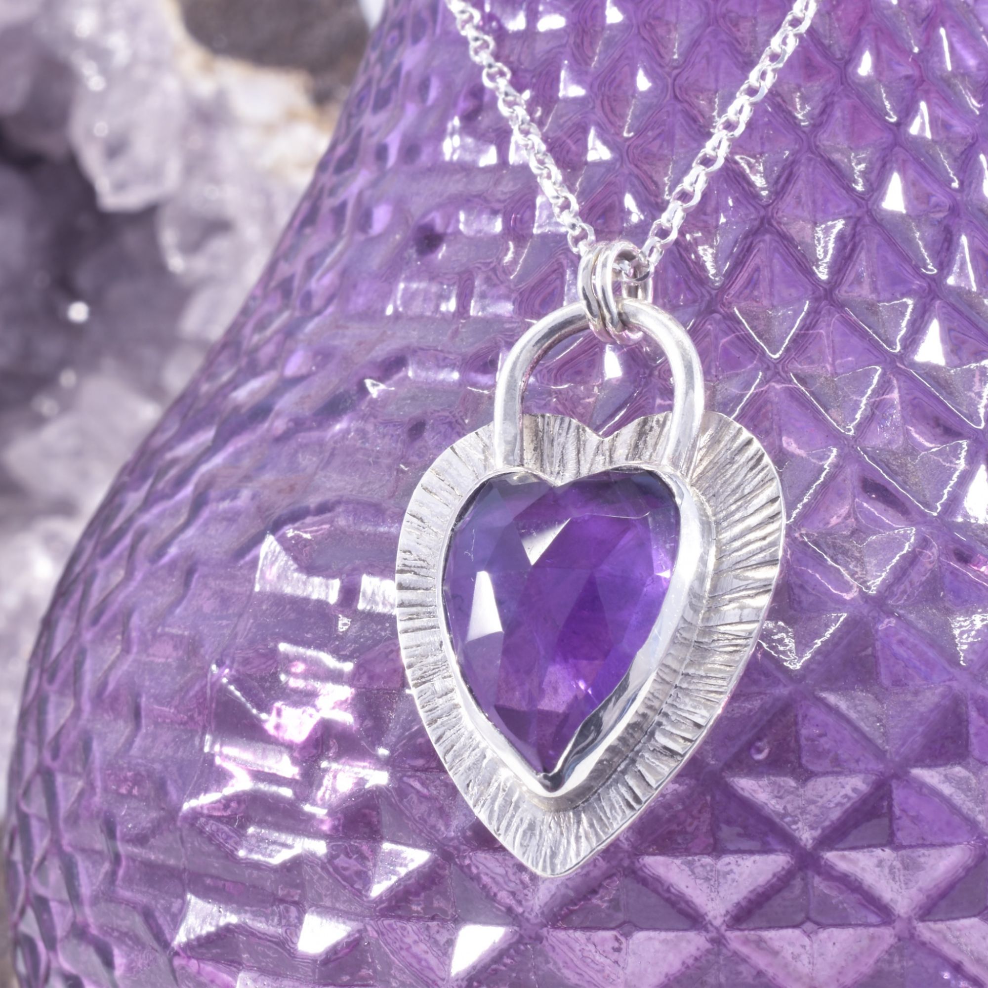 A deep purple heart of faceted amethyst, set within a hand hammered radiant silver border. A heart cut out the the reverse allows the light to shine through the stone beautifully.