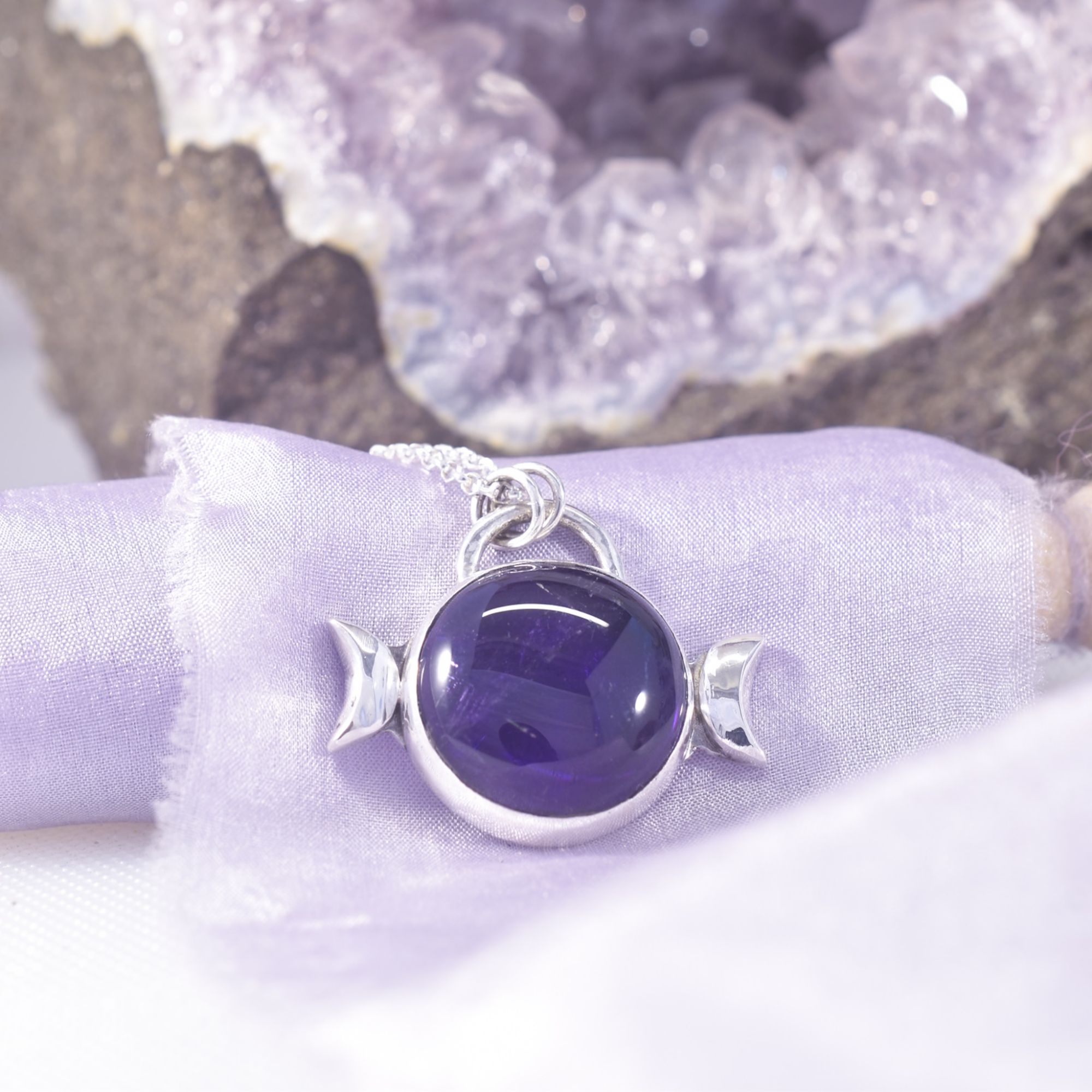 A domed disc of deep purple amethyst, captured in sterling silver and framed with a crescent moon each side, representing the triple moon.