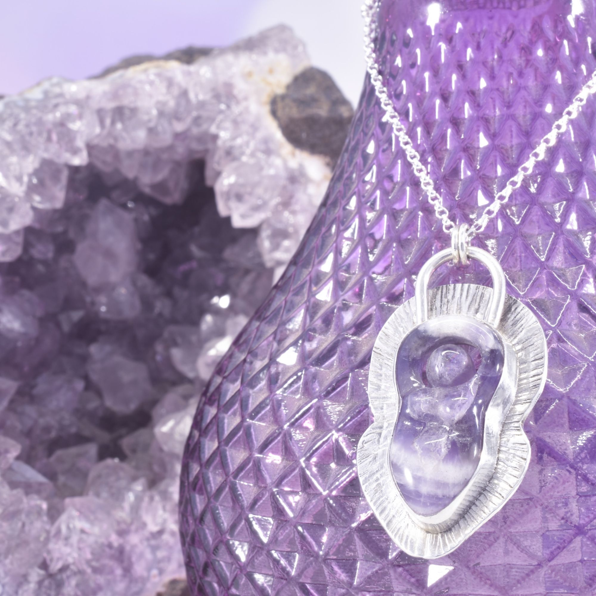 A carved amethyst goddess, set in a border of hammered, radiant lined silver, with a cut out reverse.