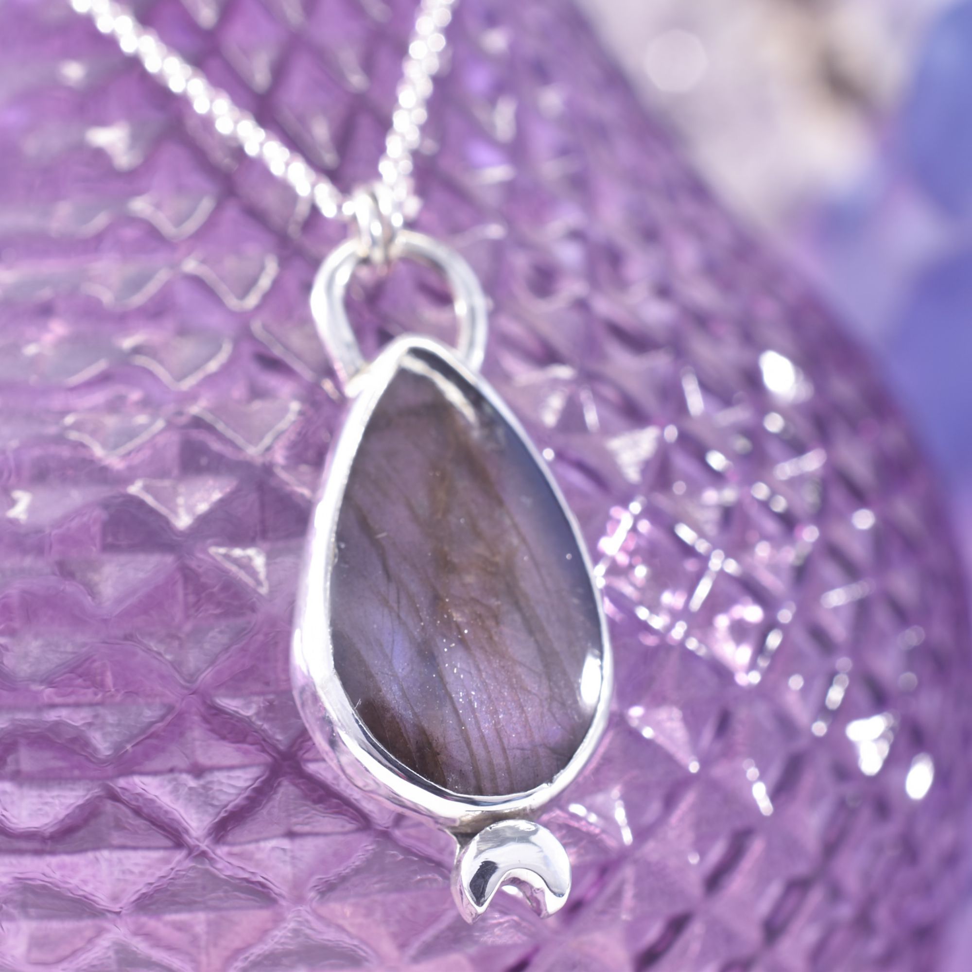 A deep purple flash labradorite teardrop encased in sterling silver, with a solid silver crescent moon to the base. A back cut out lets the light shine through this beautiful pendant.