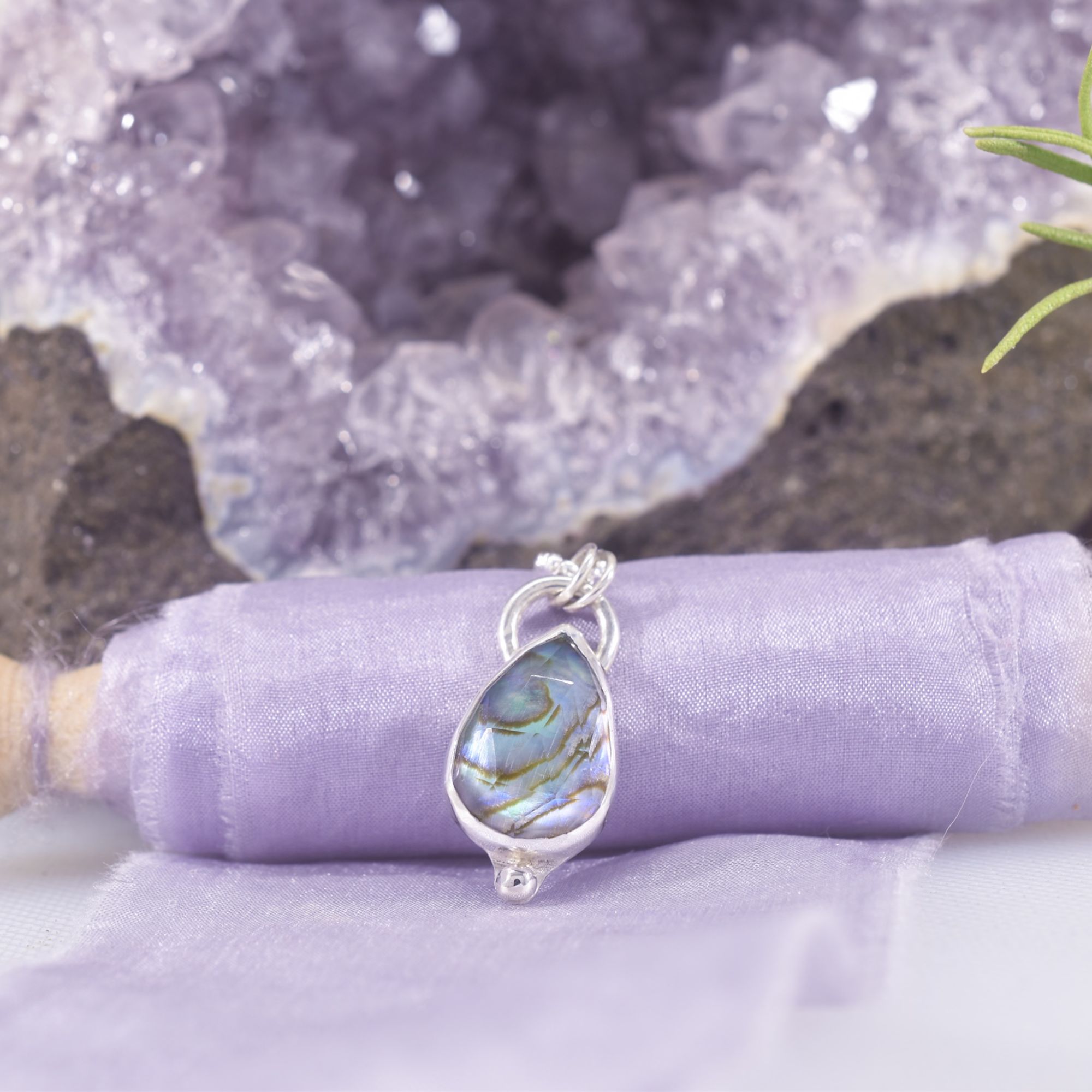 A teardrop of rainbow iridescent abalone shell with a rose cut, faceted clear quartz top, creating added sparkle. The back plate has been cut out to allow the rainbow shell to shine through. A solid silver ball sits at the base of the pendant, and a half hoop bail sits at the top with 2 soldered jump rings to attach the sparkly chain.